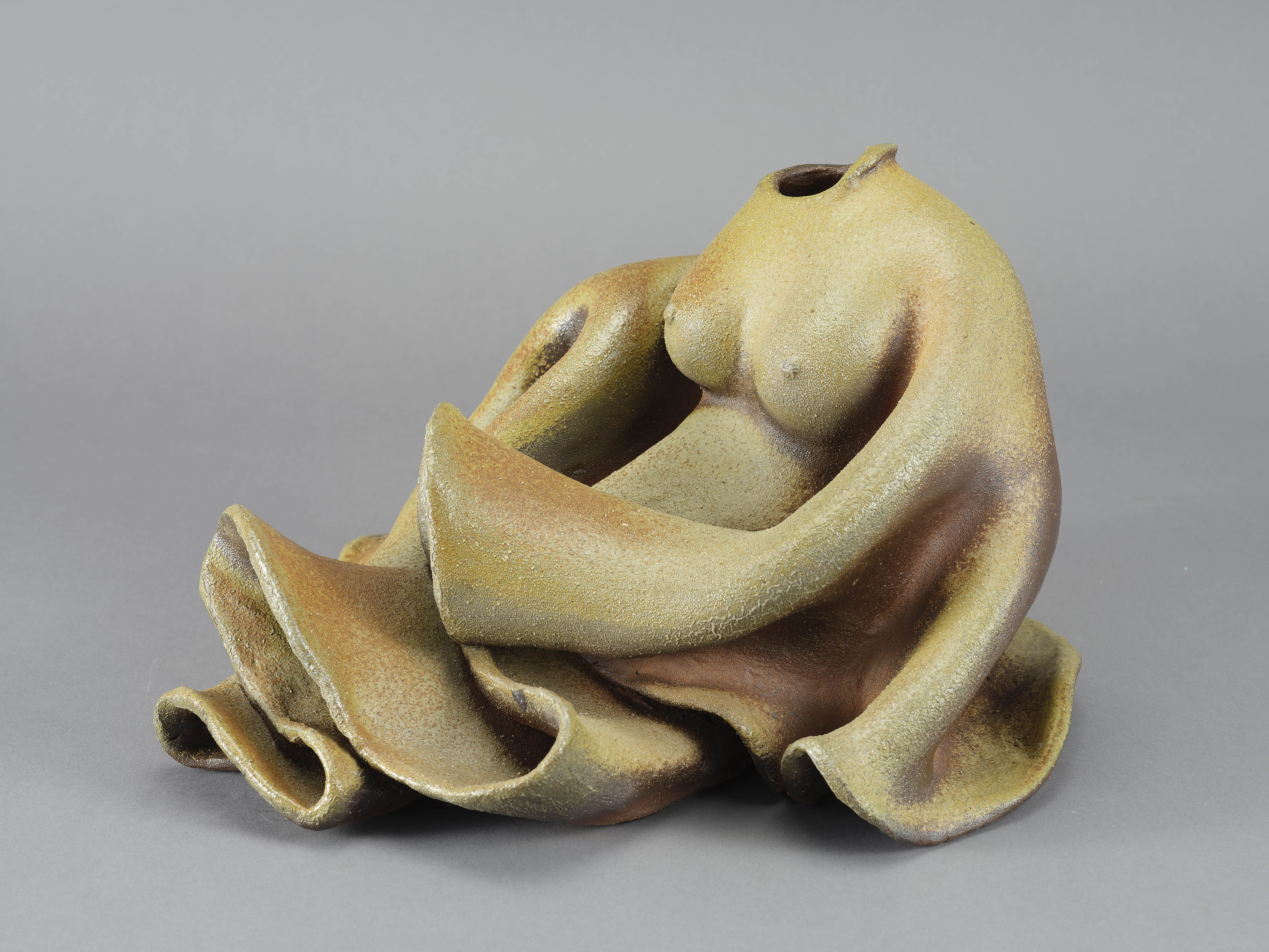 以陶塑柴燒方式表現女子婀娜姿態與衣物擬真結合的造形，整體呈現質樸，本作品並展現出具象與抽象形體之間的連結與轉化。
